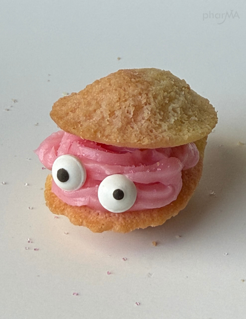 Close-up of madeleine oyster cookie with pink frosting and edible candy googly eyes.